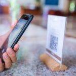 A person holding a cell phone displaying a QR code for online reviews.